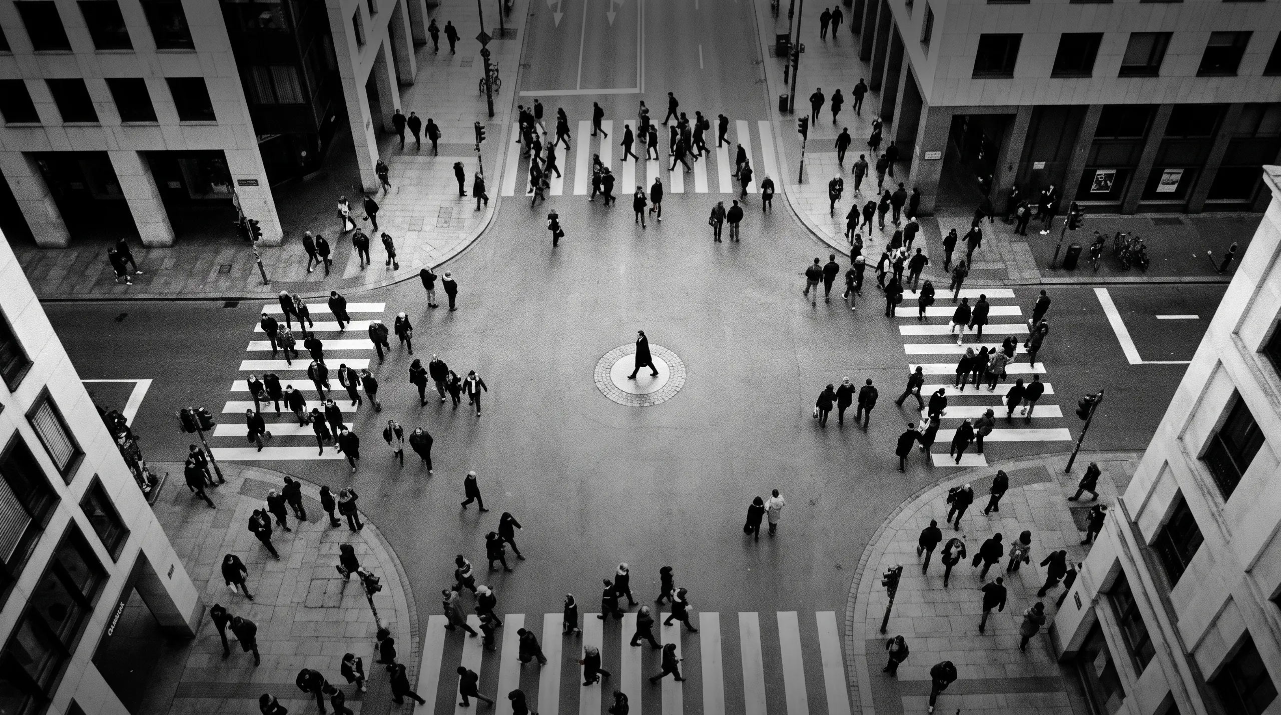 HUMAN STRUCTURES : Vue du dessus, une personne seule traverse le centre circulaire d'une place, tandis que de nombreux piétons empruntent les passages cloutés d'un carrefour animé.