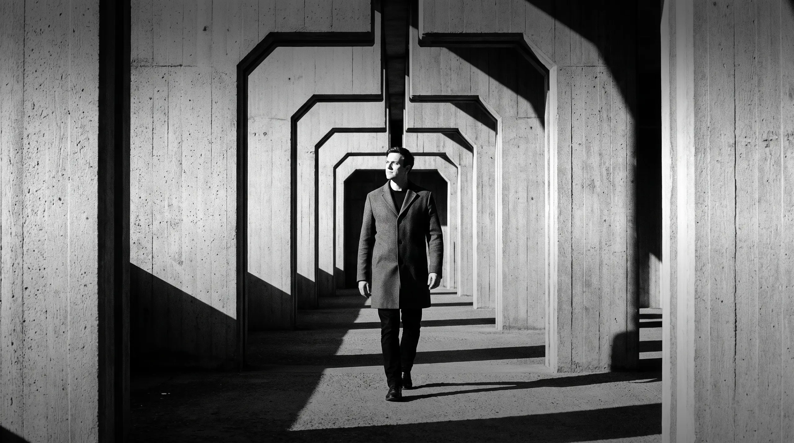 HUMAN STRUCTURES: Un homme s'avance face à l'objectif à travers une série d'arches en béton répétées, perspective symétrique alternant lumière et ombre.