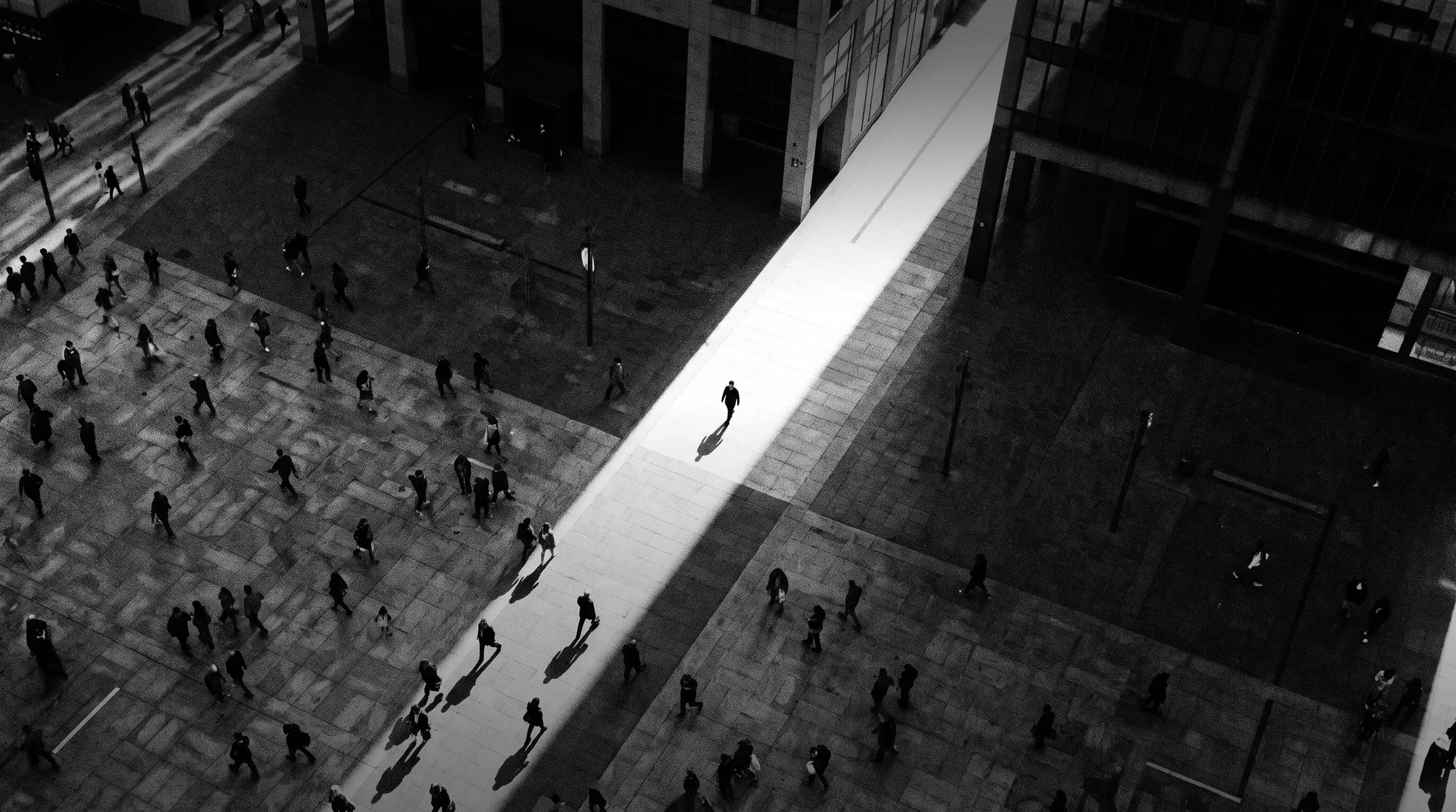 HUMAN STRUCTURES: Vue du dessus, une silhouette isolée traverse une large bande de lumière au milieu de passants sombres sur une place en béton.